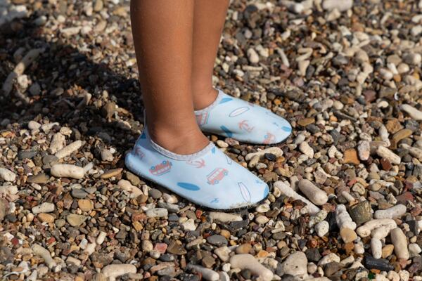 Dítě se dívá k moři, na hlavě má modrý klobouček, růžové tričko a barefoot boty do vody Playshoes. 